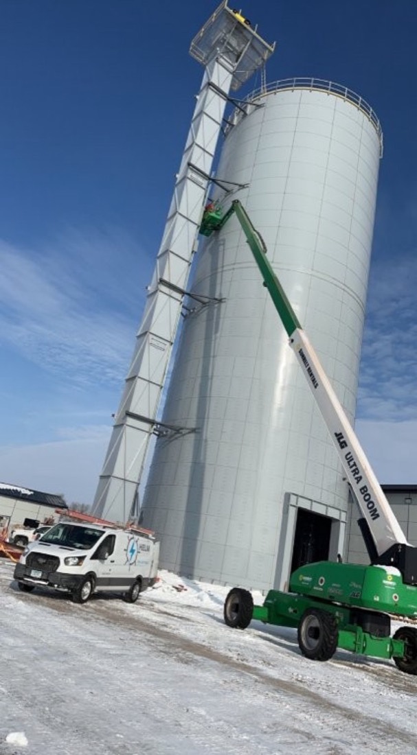 Conduit running vertically up the side of a large industrial storage tank against a blue sky.
