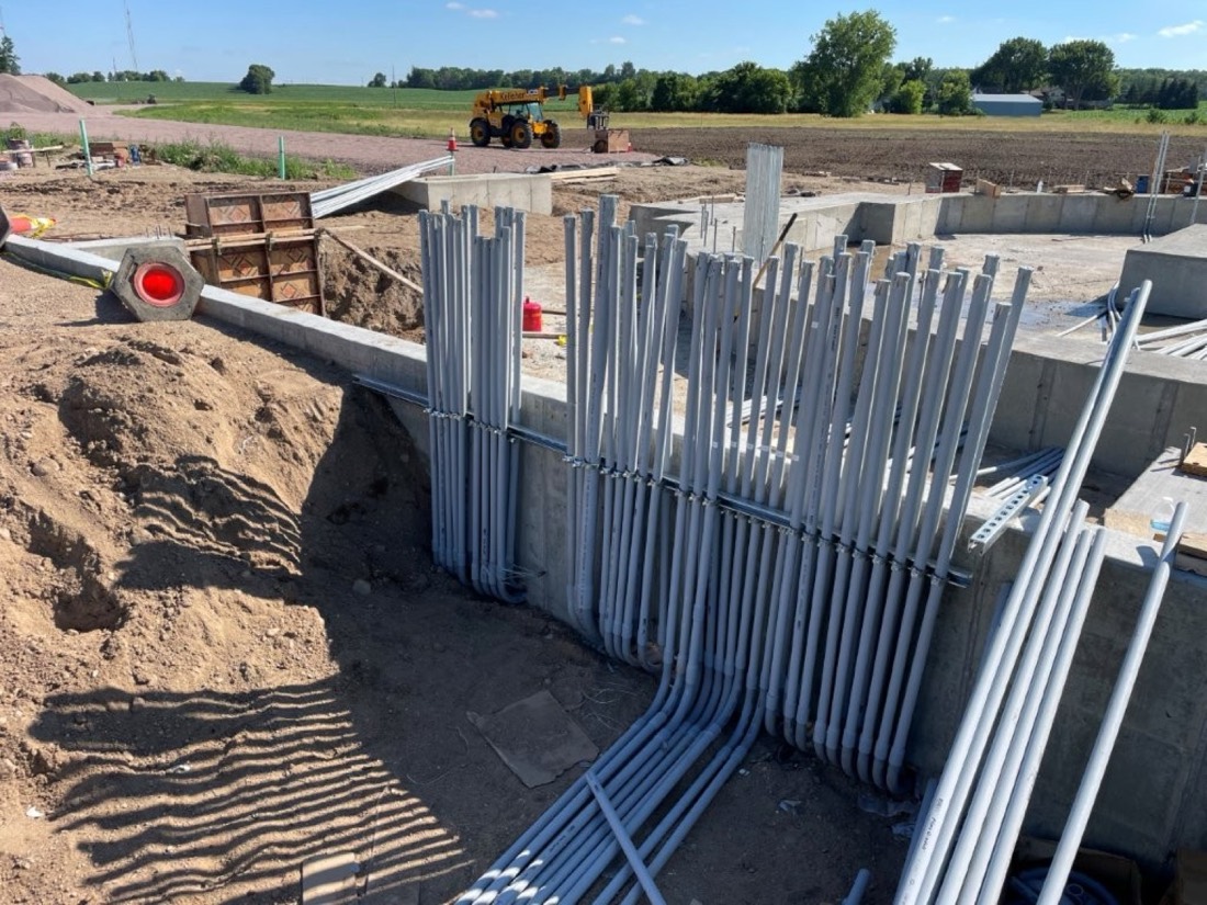 Rows of conduit stub-ups standing at a foundation wall on a construction site before the slab is poured.